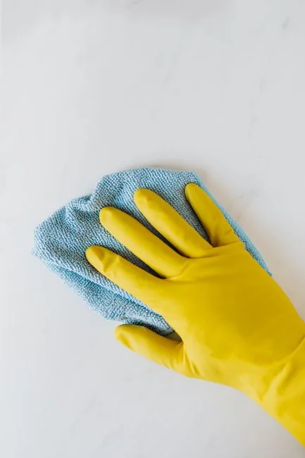 A man indoors cleaning a glass door with a spray bottle and cloth.